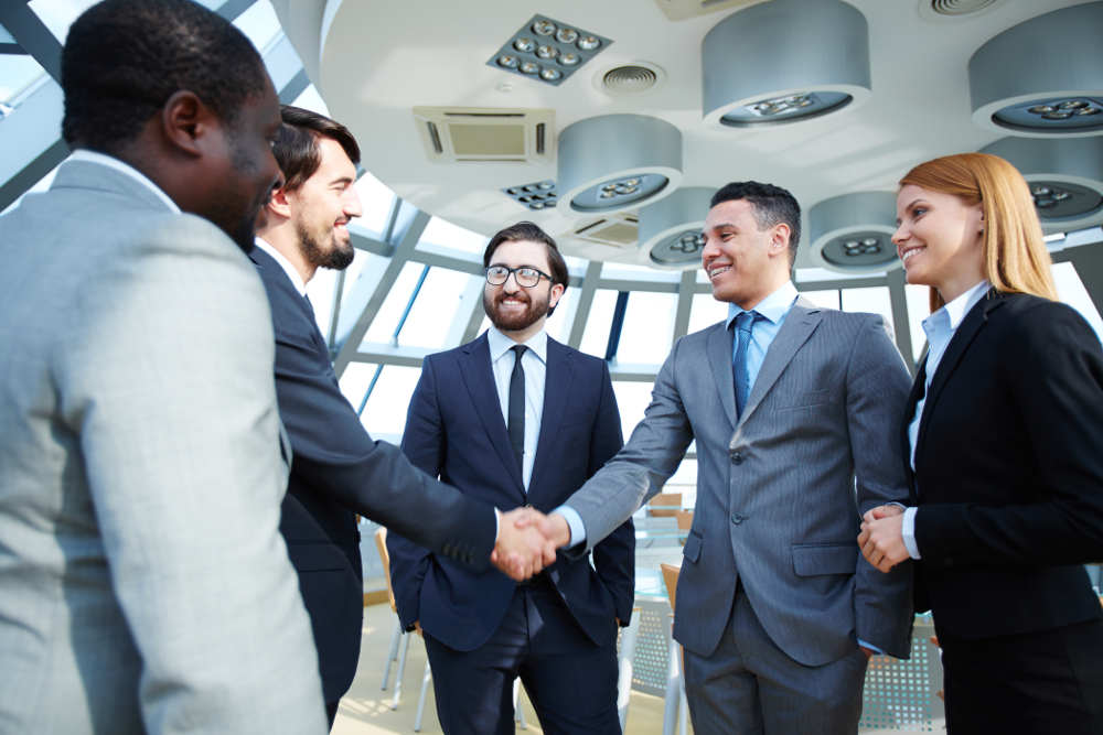 Group of business people looking at their colleagues handshaking after striking grand deal